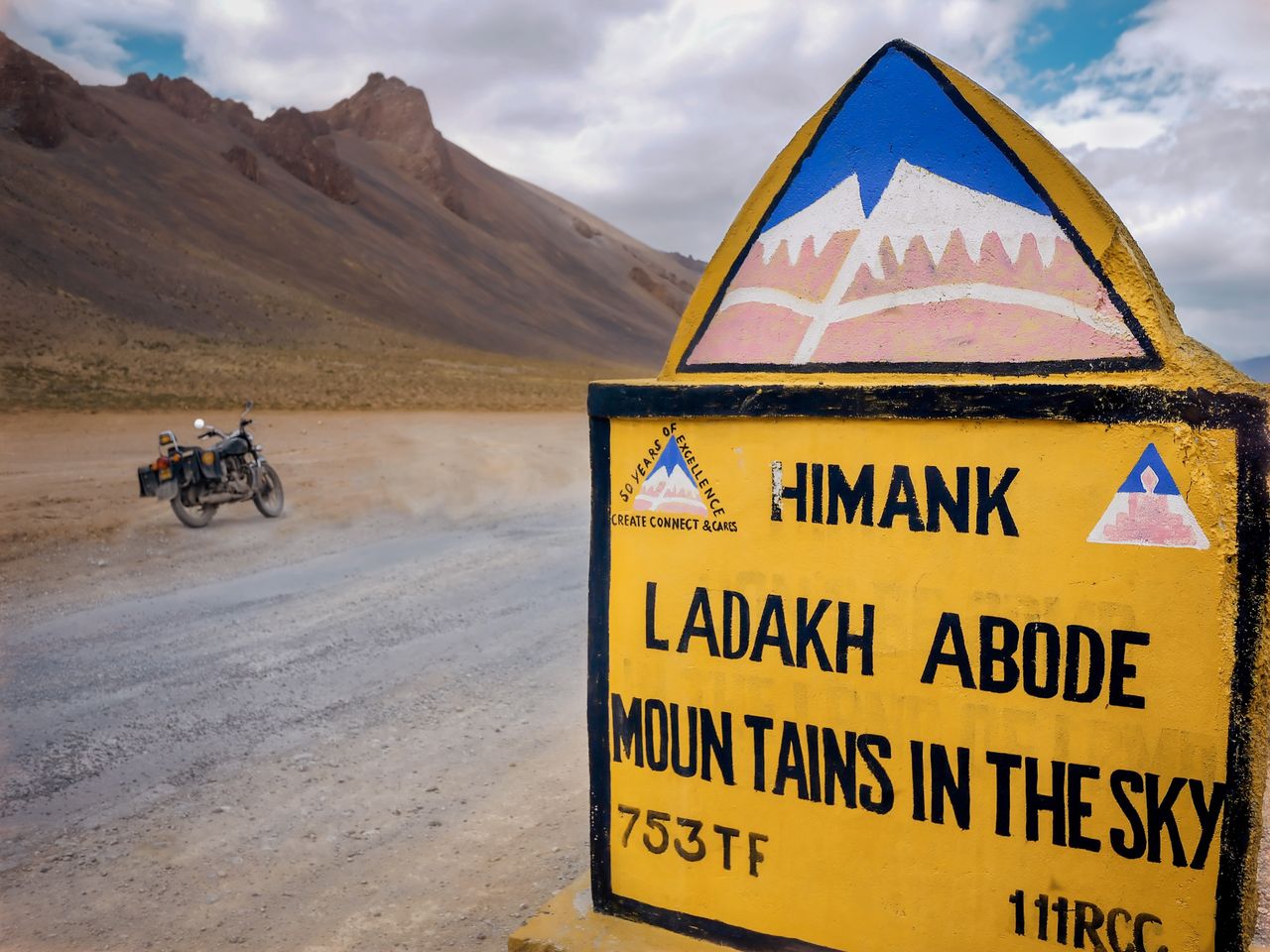 Road sign in Ladakh with motorcycle. Vast scenic mountain landscape ideal for adventure travel.