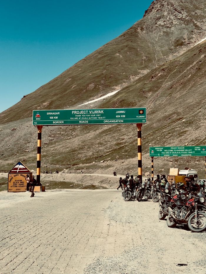 Group of motorcyclists at the entrance of Zojila Pass under a clear blue sky.